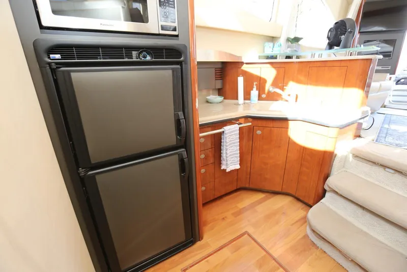 Slide: The Image of 2004 Sea Ray 420 Sedan Bridge kitchen with microwave, fridge, and wooden cabinetry. - 75