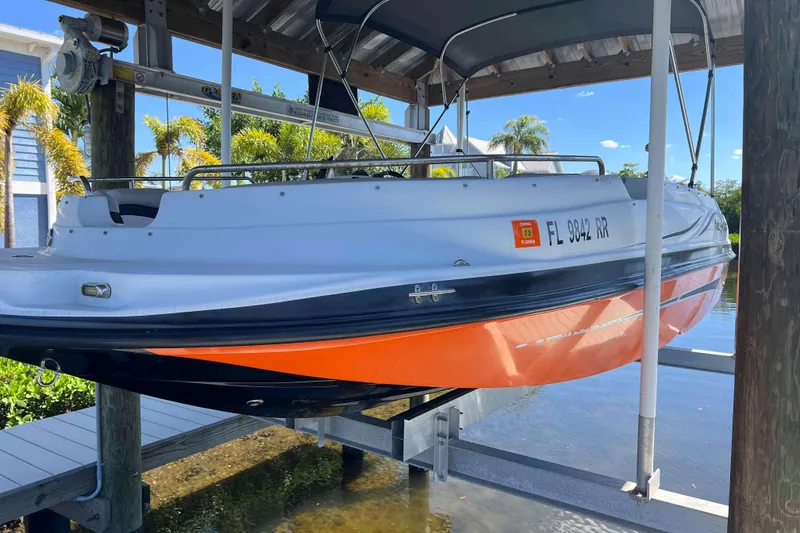 Slide: The Image of 2018 Starcraft SVX 190 OB boat on lift, orange hull, docked in sunny setting. - 9