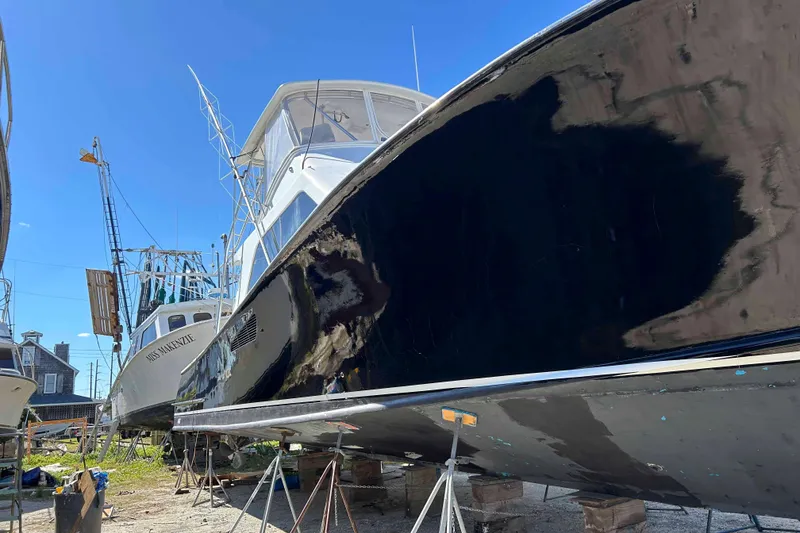 Slide: The Image of 1984 Tiffany 50 Convertible yacht on dry dock, with a sleek black hull under a clear blue sky. - 8