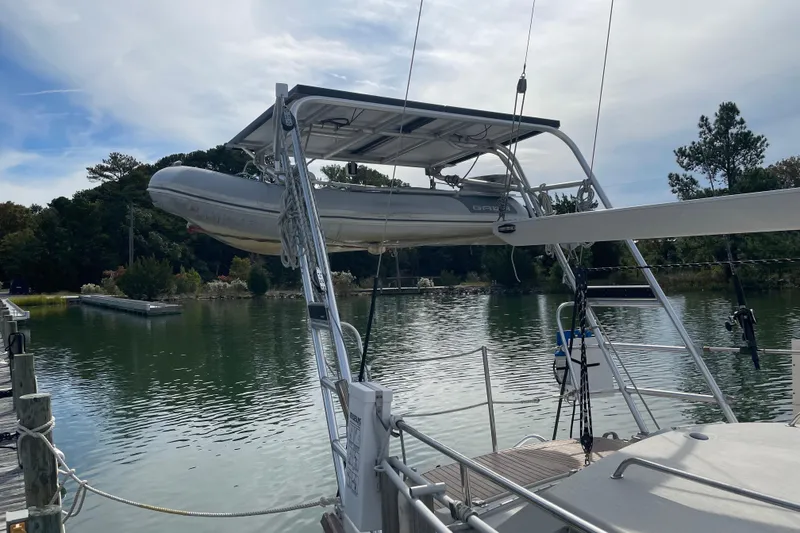 Slide: The Image of Sailboat Amel Santorin 1993 with dinghy, docked by a serene lake under a cloudy sky. - 38