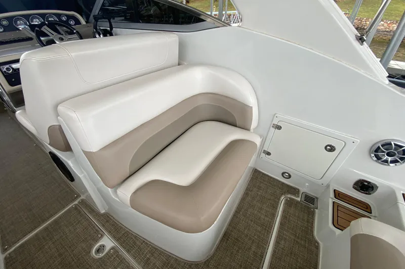 Slide: The Image of 2015 Crownline 335 SS boat interior with beige seating and dashboard, docked by the water. - 16