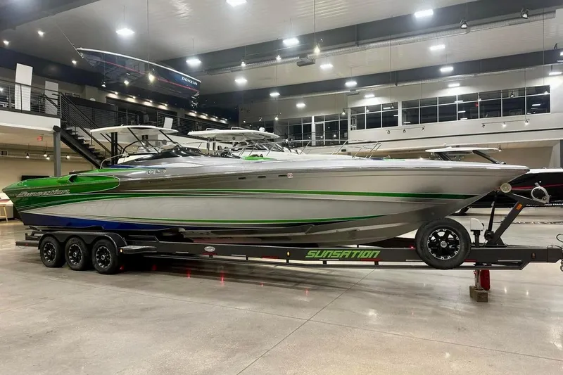 Slide: The Image of 2013 Sunsation 36 XRT speedboat with green and silver design on a trailer outside a building. - 2