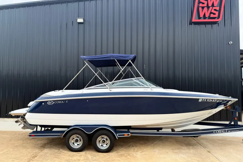 The Image of 2005 Cobalt 240 boat with blue and white design on a trailer, parked outside a building. - 0