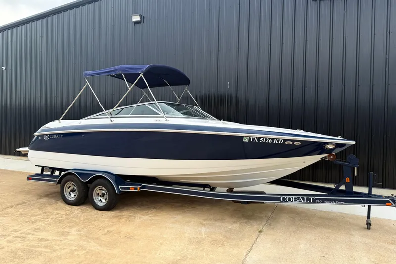 Slide: The Image of 2005 Cobalt 240 boat on trailer, parked by a black building. - 1