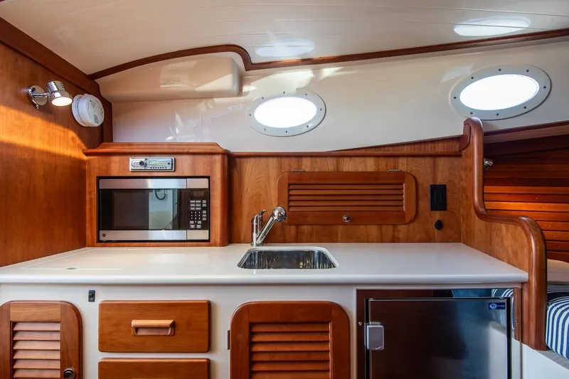 Slide: The Image of Hinckley Talaria 34 yacht interior, featuring a compact kitchen with wood cabinetry and modern appliances. - 20