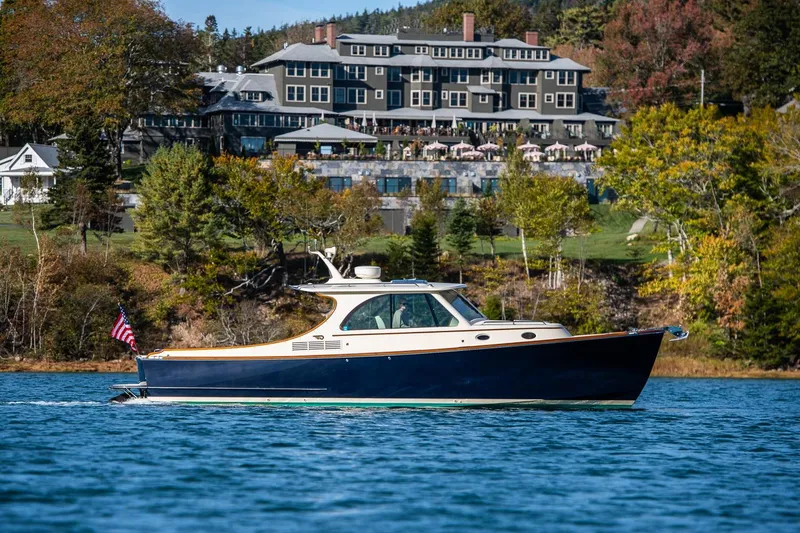 Slide: The Image of 2013 Hinckley Talaria 34 cruising on a scenic lake with a grand hotel backdrop. - 30