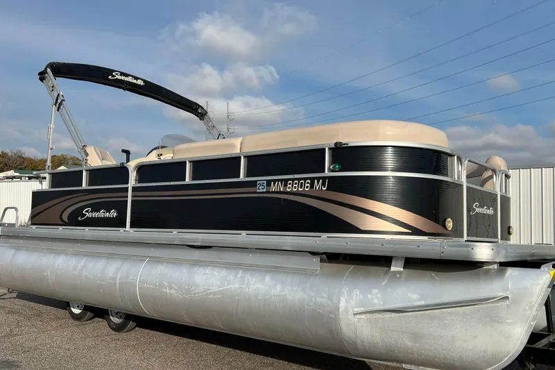 The Image of 2013 Godfrey Sweetwater 2286 pontoon boat with black and beige design, parked outdoors. - 0