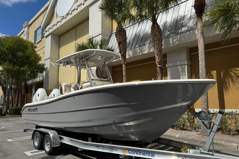Slide: The Image of 2026 Bulls Bay 255CC boat on trailer, parked near palm trees and building. - 2
