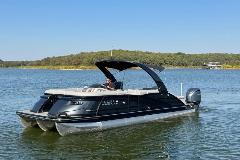 Slide: The Image of 2023 Bennington QX 27 QXSBAX2 pontoon boat cruising on a serene lake. - 2