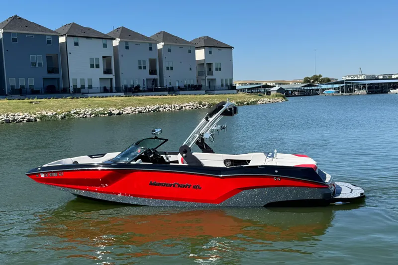 The Image of 2021 MasterCraft NXT24 boat on a calm lake near modern houses. - 1