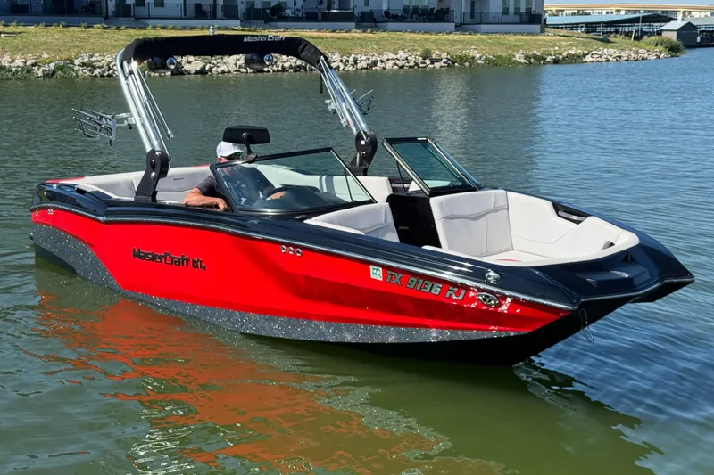 Slide: The Image of 2021 MasterCraft NXT24 boat in red and black on a calm lake. - 2