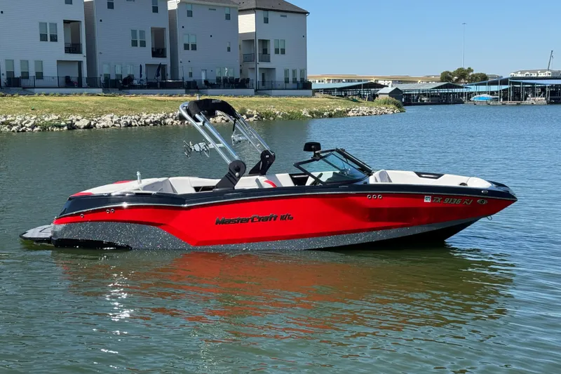 Slide: The Image of 2021 MasterCraft NXT24 boat in vibrant red on a calm lake near modern buildings. - 4