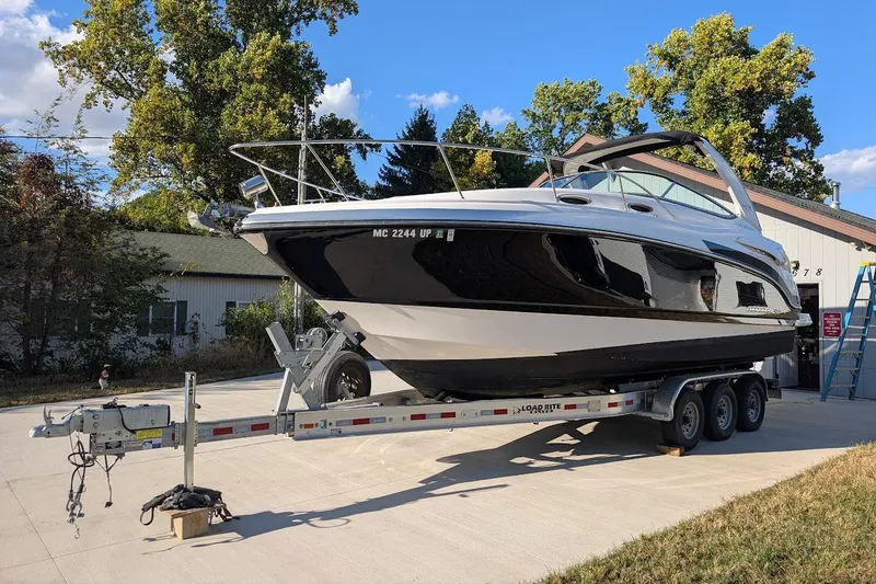 Slide: The Image of 2016 Chaparral 290 Signature boat on trailer, parked outdoors near trees and building. - 2