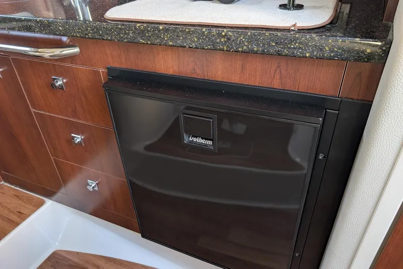 Slide: The Image of 2016 Chaparral 290 Signature interior with wood cabinetry and compact fridge. - 23