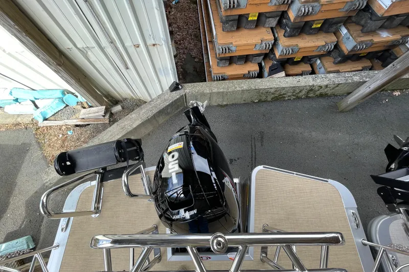 Slide: The Image of 2026 Harris Cruiser 210 boat with Mercury 150 engine, docked near stacked materials. - 6