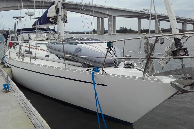 The Image of 1980 Nordic 44 sailboat docked near a bridge, featuring a dinghy on deck. - 0