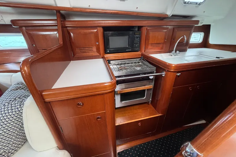 Slide: The Image of 2002 Beneteau Oceanis 411 yacht kitchen with wood cabinetry, stove, microwave, and sink. - 24