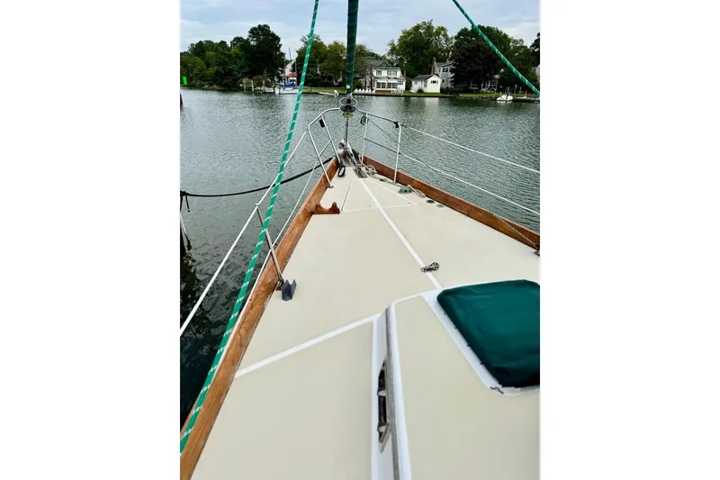 Slide: The Image of 1981 Bristol 45.5 Aft Cockpit sailboat on calm water, surrounded by trees and houses. - 4