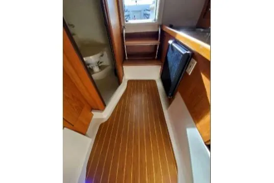 Slide: The Image of 1999 Mainship Pilot 30 interior with wood flooring, compact kitchen, and storage shelves. - 20