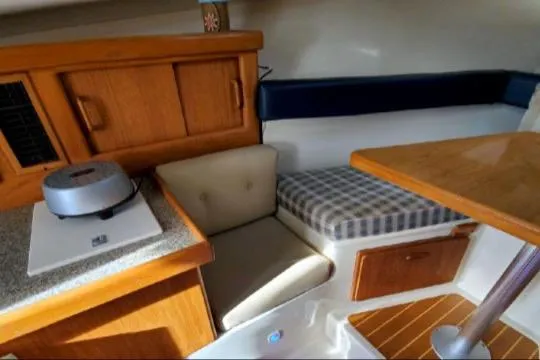 Slide: The Image of 1999 Mainship Pilot 30 cabin interior with seating, table, and wooden cabinetry. - 23