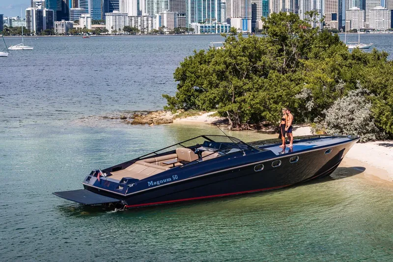 Slide: The Image of Magnum 50 Bestia yacht docked on a sandy shore with city skyline backdrop. - 45
