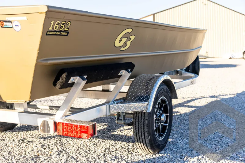 Slide: The Image of 2026 G3 1652 VBW boat on trailer, parked on gravel near a building. - 17