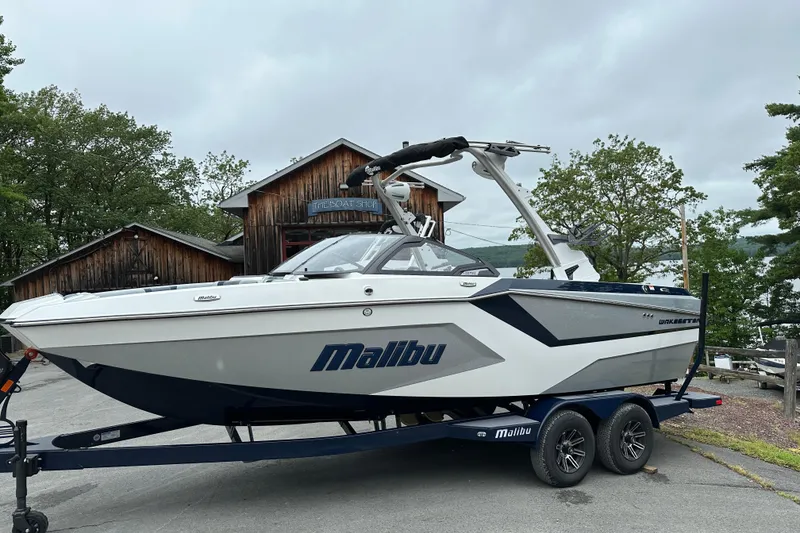 The Image of 2025 Malibu Wakesetter 22 MXZ boat on trailer, parked near rustic buildings. - 0