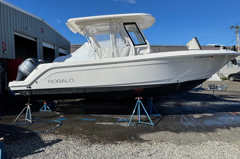 The Image of 2019 Robalo R272 Center Console boat on stands outside a garage. - 0