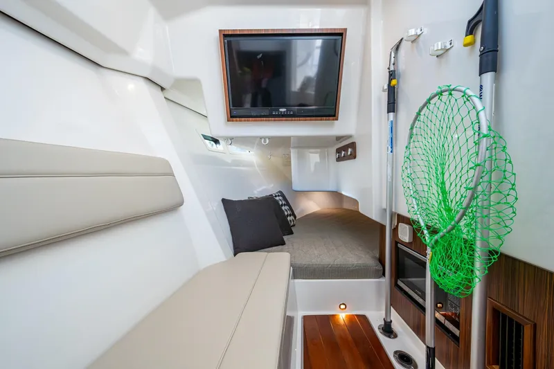 Slide: The Image of 2019 Pursuit DC 365 Dual Console cabin interior with seating, TV, and fishing gear. - 10