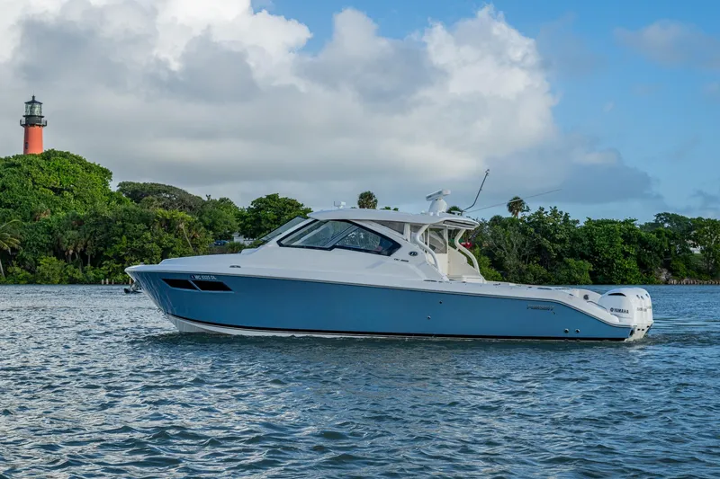 Slide: The Image of 2019 Pursuit DC 365 Dual Console boat on water near lush greenery and lighthouse. - 46