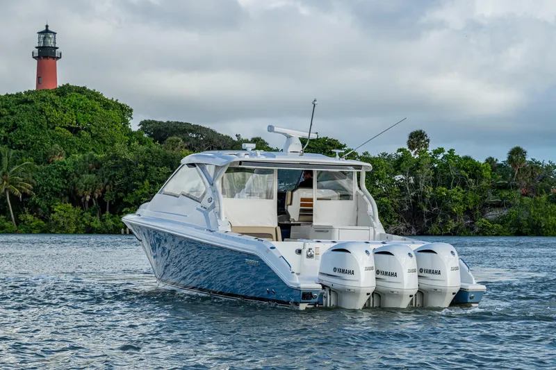 Slide: The Image of 2019 Pursuit DC 365 Dual Console boat on water near lush greenery and lighthouse. - 48