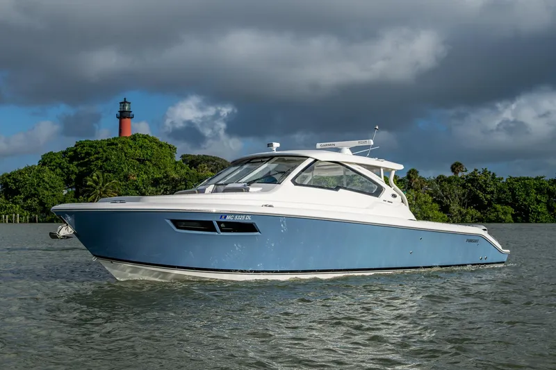 Slide: The Image of 2019 Pursuit DC 365 Dual Console boat on water near lush greenery and lighthouse. - 53