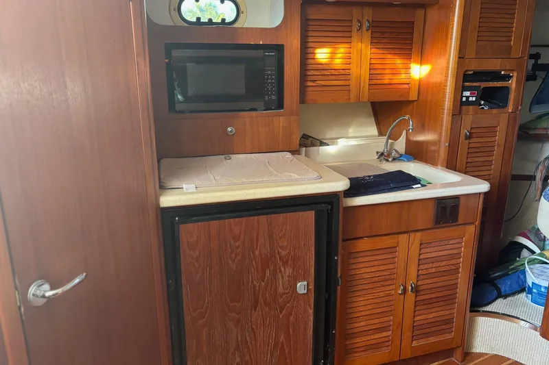 Slide: The Image of 2000 Pursuit 3400 Express boat interior with fishing gear and seating, docked by palm trees. - 23