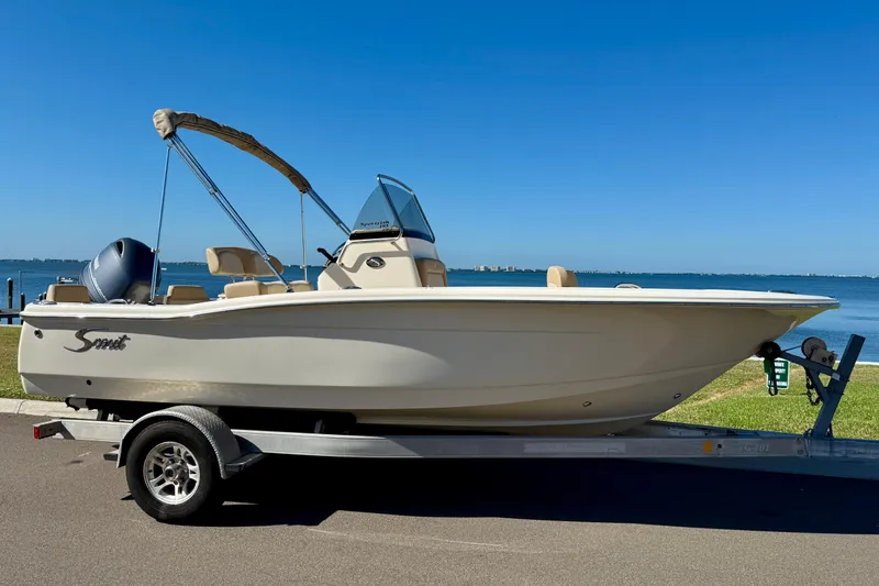 The Image of 2026 Scout 195 Sportfish boat on trailer by the waterfront under clear blue sky. - 0