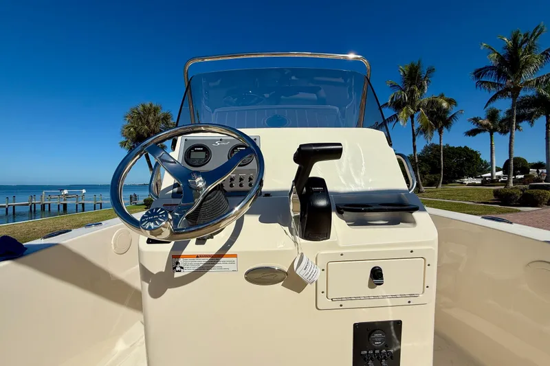 Slide: The Image of 2026 Scout 195 Sportfish boat dashboard with steering wheel, throttle, and clear blue sky background. - 16