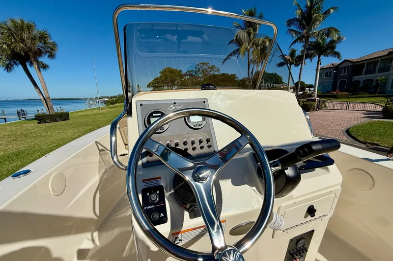 Slide: The Image of 2026 Scout 195 Sportfish boat dashboard with steering wheel, set against a scenic waterfront. - 17