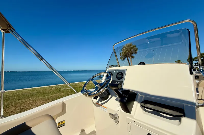 Slide: The Image of 2026 Scout 195 Sportfish boat interior with steering wheel, overlooking serene waterfront. - 19