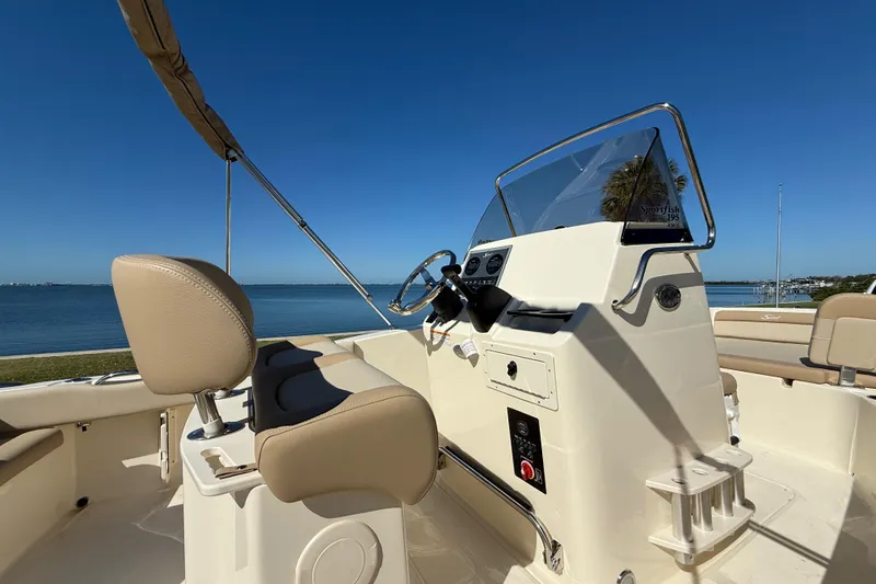 Slide: The Image of 2026 Scout 195 Sportfish boat interior with steering console and seating, overlooking serene waters. - 27
