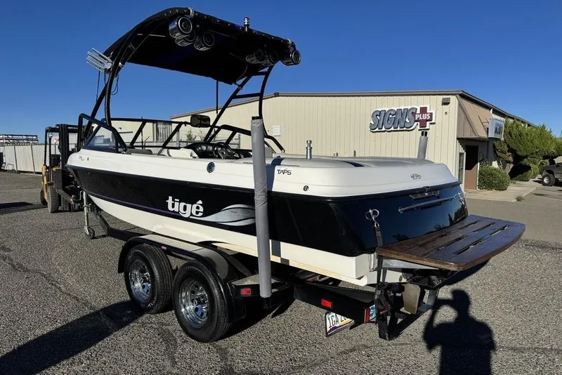 Slide: The Image of 1999 Tigé 2100V Limited boat on trailer, parked outside a building under clear blue sky. - 61