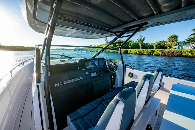 Slide: The Image of 2021 Axopar 37 boat interior with modern dashboard, steering wheel, and seating on a sunny day. - 24