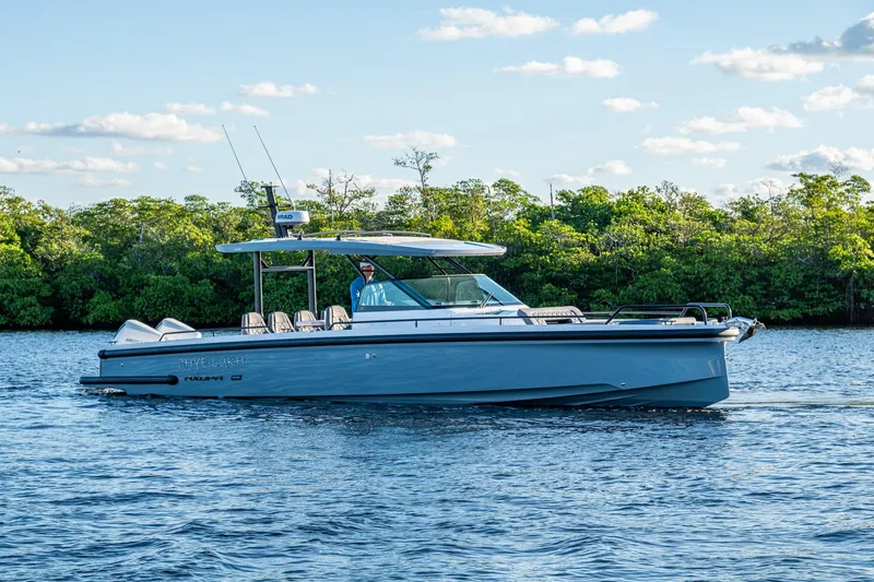 Slide: The Image of 2021 Axopar 37 boat cruising on a calm lake with lush green trees in the background. - 45