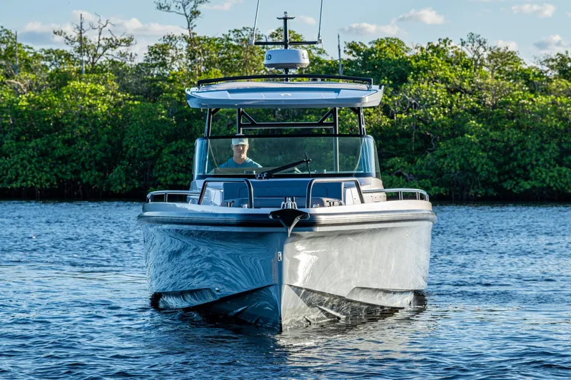 Slide: The Image of 2021 Axopar 37 boat cruising on a calm lake with lush greenery in the background. - 48