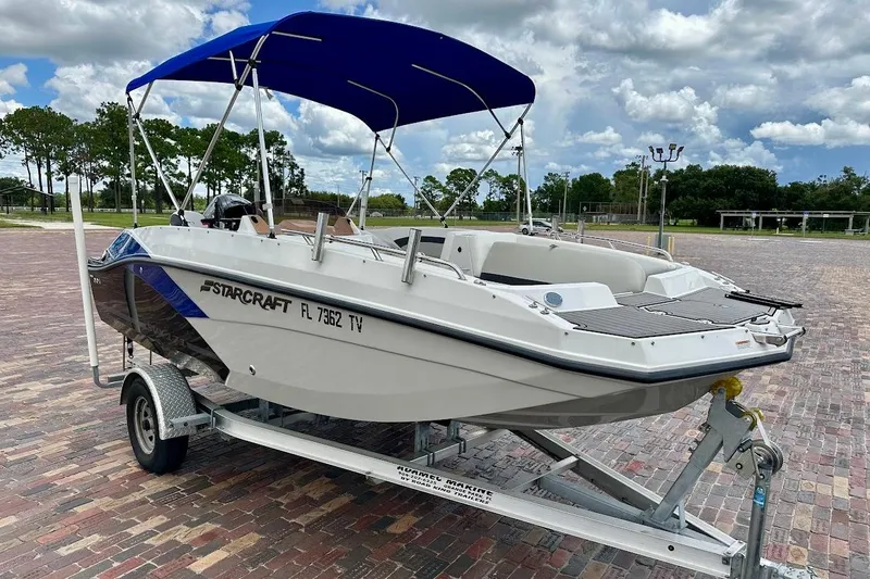 Slide: The Image of 2023 Starcraft SVX 171 OB boat on trailer with blue canopy, parked on brick pavement. - 2