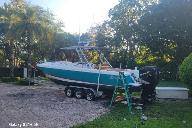 Slide: The Image of 2005 Intrepid 323 Cuddy boat on trailer with Mercury outboard, surrounded by lush greenery. - 12