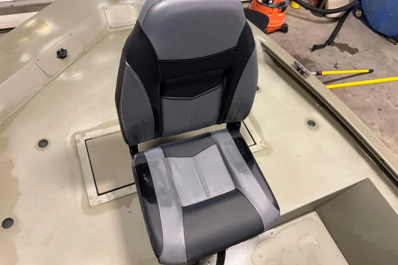 Slide: The Image of 2024 Tracker Grizzly 1648 SC boat seat, gray and black design, in a workshop setting. - 12