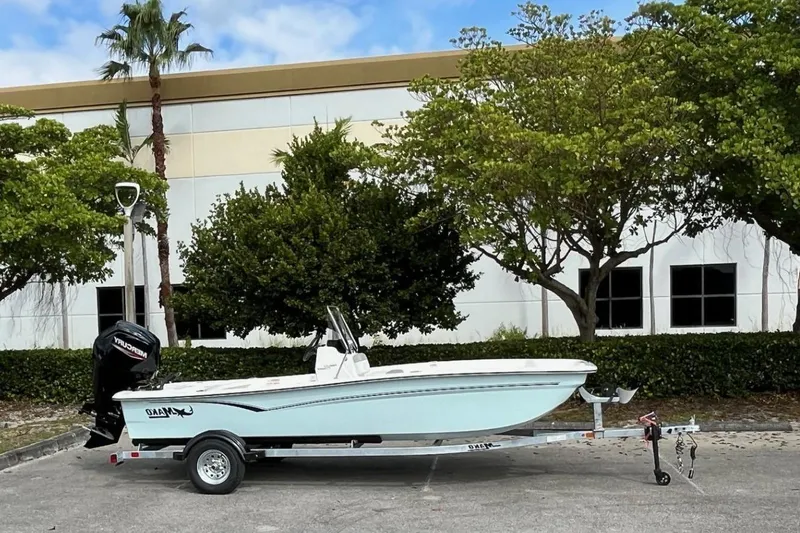 Slide: The Image of 2026 Mako Pro Skiff 17 CC boat on trailer, parked near trees and building. - 1
