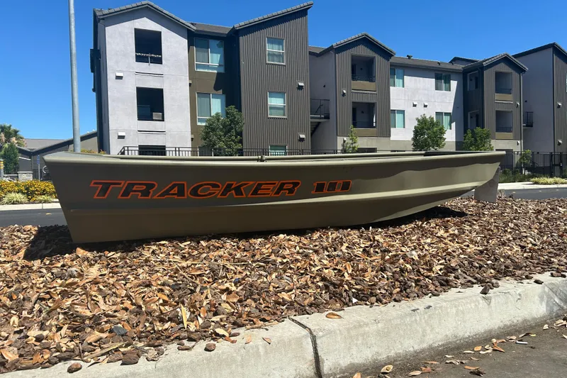 Slide: The Image of 2026 Tracker Grizzly 10 Jon boat displayed outdoors near modern apartments. - 2