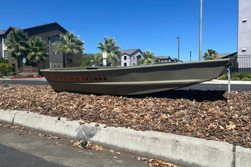 Slide: The Image of 2026 Tracker Grizzly 10 Jon boat displayed on landscaped area near apartments. - 3