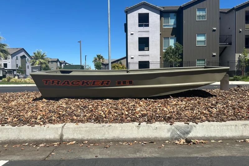 The Image of 2026 Tracker Grizzly 10 Jon boat displayed outdoors near modern apartments. - 0