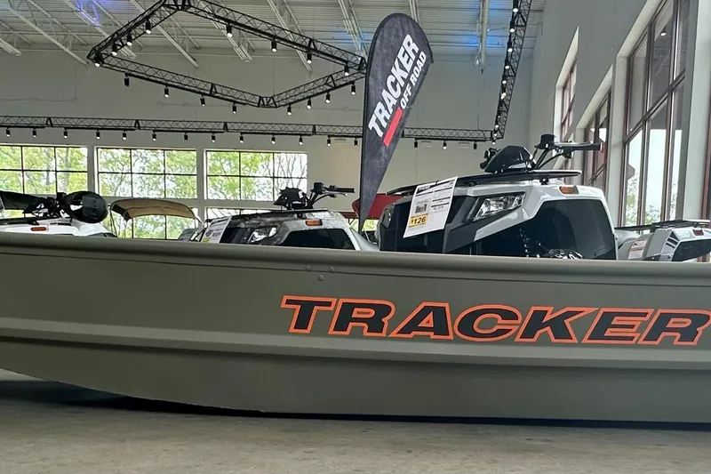 The Image of 2026 Tracker Grizzly 10 Jon boat displayed indoors with off-road vehicles. - 0